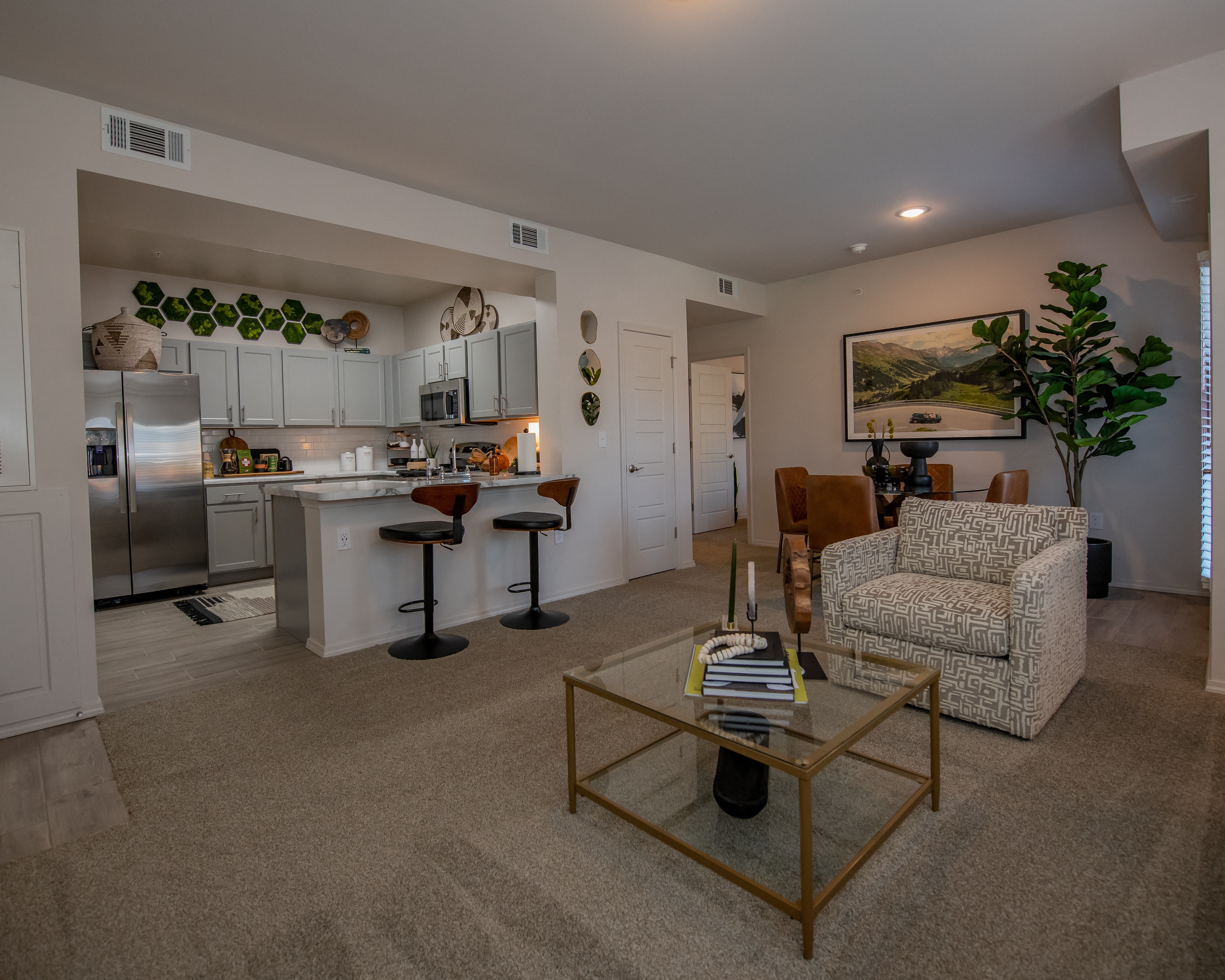 a living room with a glass coffee table in front of a kitchen